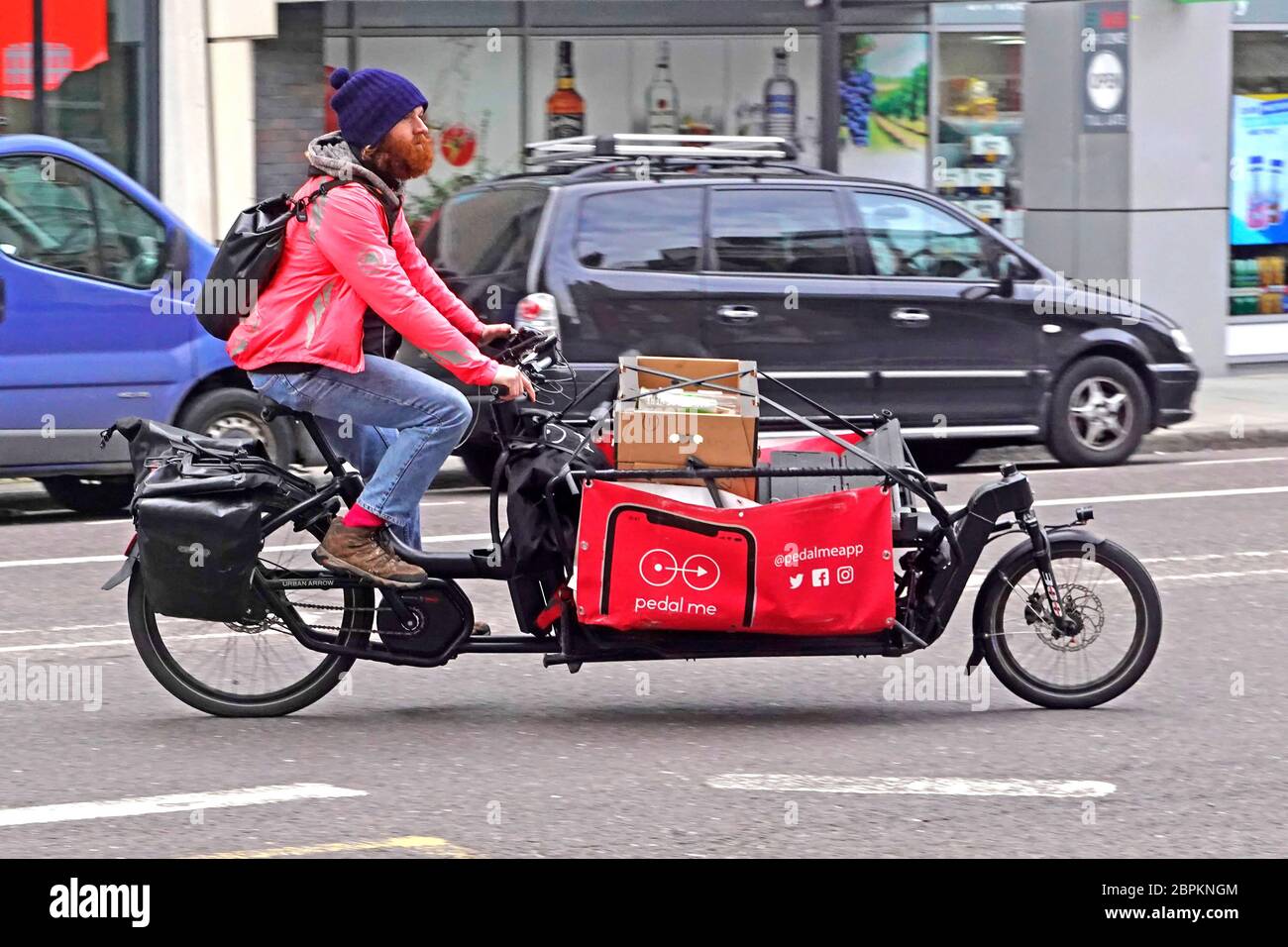 Seitenansicht einer PedalMe-App führte zu einer neuen Geschäftsidee mit rotem Cargo-Bike und männlichem Fahrer, um eine Paketzustellung im Zentrum von London, England, zu machen Stockfoto