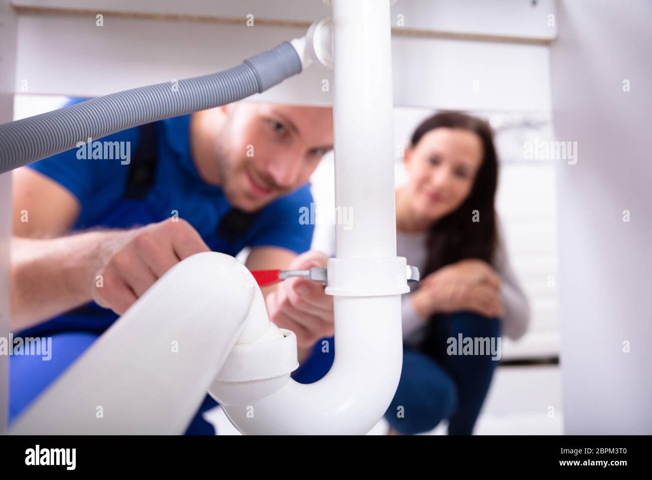 Junge Frau mit männlichen Klempner zur Festsetzung Waschbecken Rohr in der Küche Stockfoto