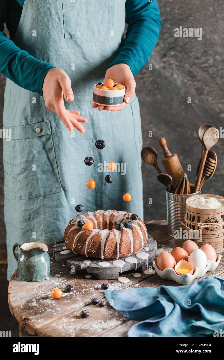 Weibliche Hände gießen Beeren auf ostern Hefe Kuchen auf Holzplatte Stockfoto