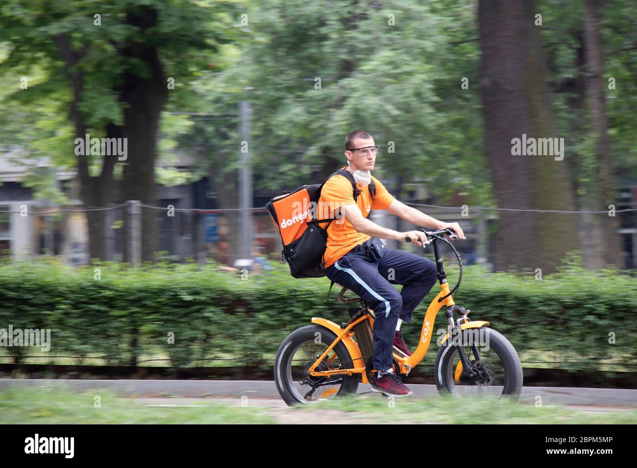 Belgrad, Serbien - 15. Mai 2020: Junger Kurier-Service der Stadt fährt ein elektrisches orangenes Fahrrad im Stadtpark Stockfoto