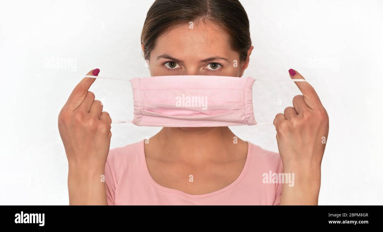 Junge Frau, die rosa Baumwolle Hause gemacht Virus Mund Gesichtsmaske auf, hält es vor ihr, Porträt auf weißem Hintergrund, kann während coron verwendet werden Stockfoto
