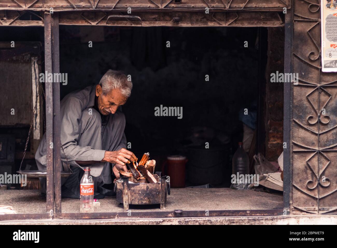 Ein alter Mann, der im Winter Feuer für Hitze in seinem Laden in Lahore Pakistan anzündet Stockfoto