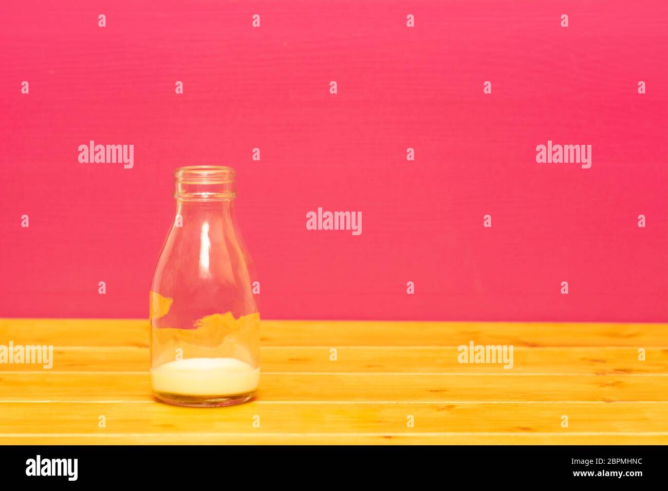 Ein Drittel pint Glas Milch Flasche mit Abschaum der Banane Milchshake, auf einen hölzernen Tisch gegen eine rosa gemalten Hintergrund Stockfoto