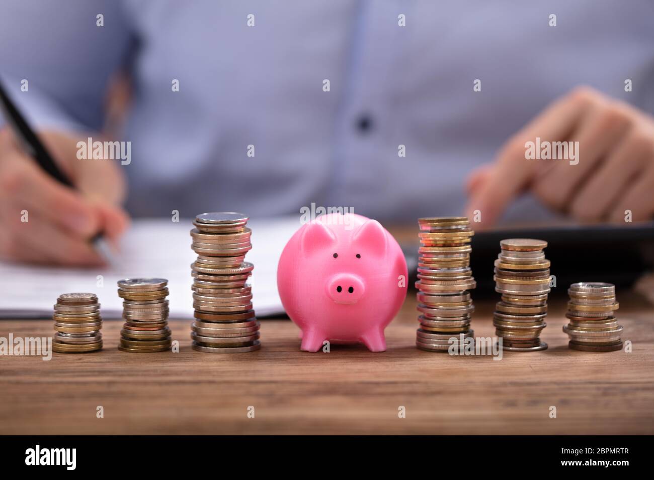Gestapelte Münzen und rosa Sparschwein Vor Geschäftsmann Berechnung Rechnung auf hölzernen Schreibtisch Stockfoto