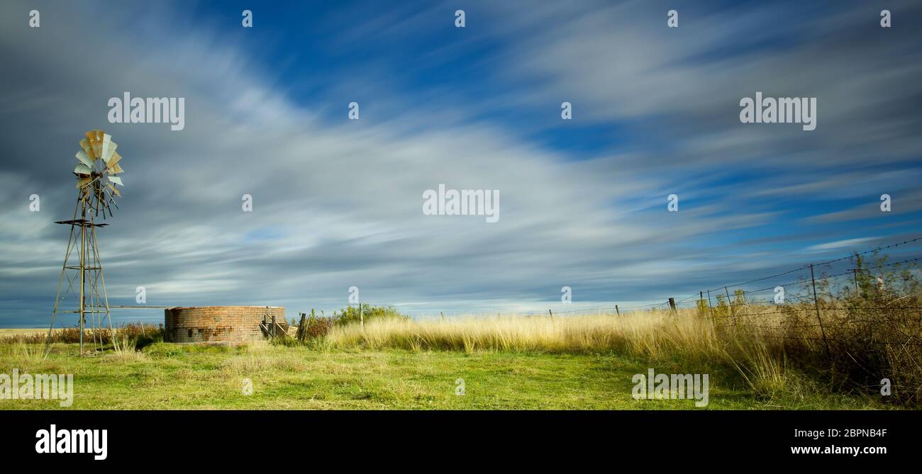 Langbelichtungs-Bild mit Windmühle und Damm und streifigen Wolken über dem Kopf Stockfoto