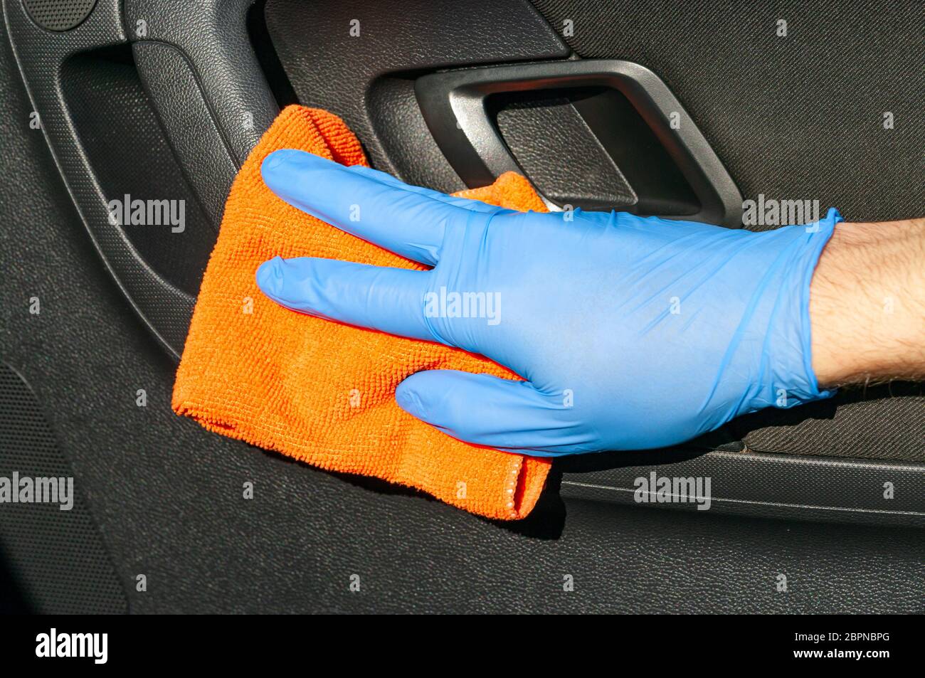 Die Hand des Fahrers in blauem Schutzhandschuh wischt mit einem Tuch einen Innentürgriff der Autotür ab. Coronavirus oder Covid-19 Autodesinfektion Stockfoto