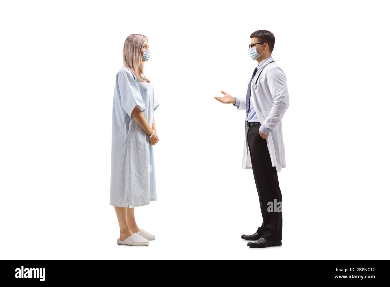In voller Länge: Aufnahme einer Patientin in einem Krankenhauskleid und eines Arztes, der auf weißem Hintergrund isoliert spricht und Schutzmasken trägt Stockfoto