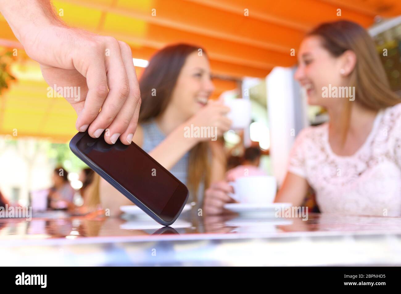 Abgelenkt Freunde sprechen in einer Bar und Nahaufnahme der Hand ein Dieb Diebstahl Telefon in Vordergrund Stockfoto