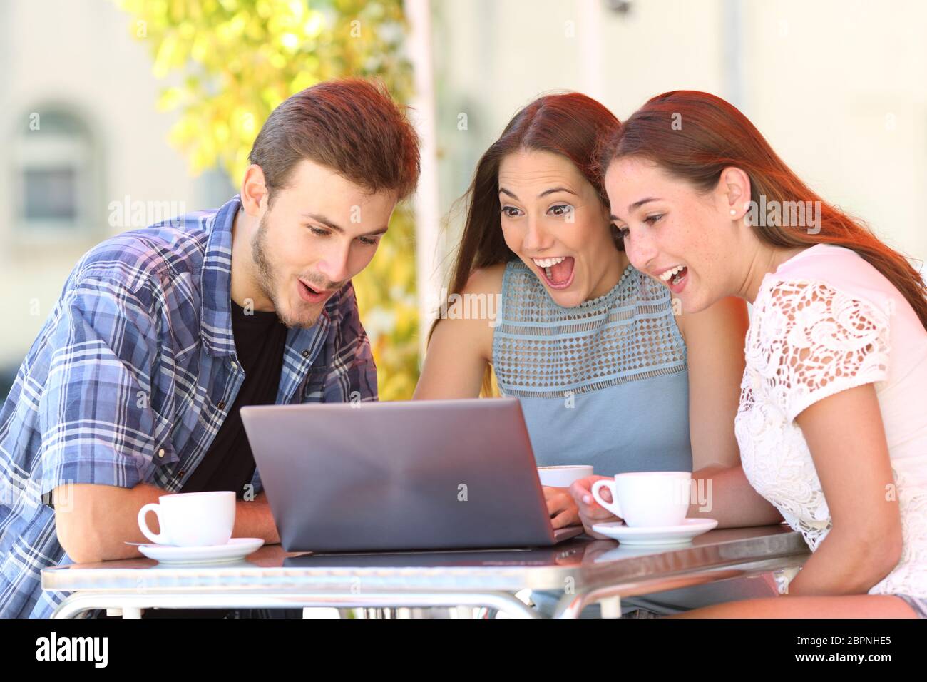 Drei überrascht Friends Online die Inhalte auf den Laptop in einem Coffee Shop Stockfoto