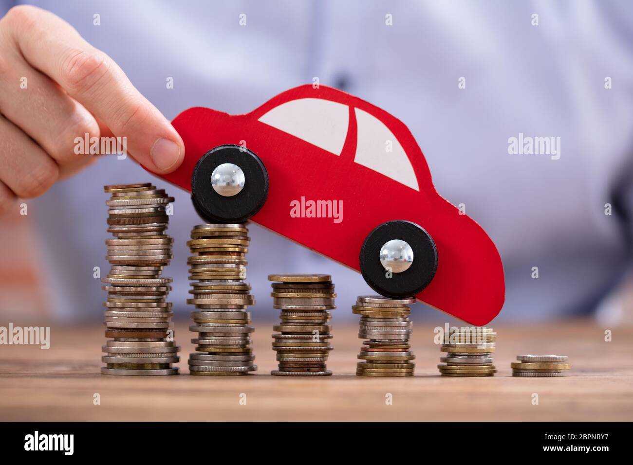 Nahaufnahme einer Hand, die einer Person Auto über Rückläufige gestapelte Münzen Stockfoto
