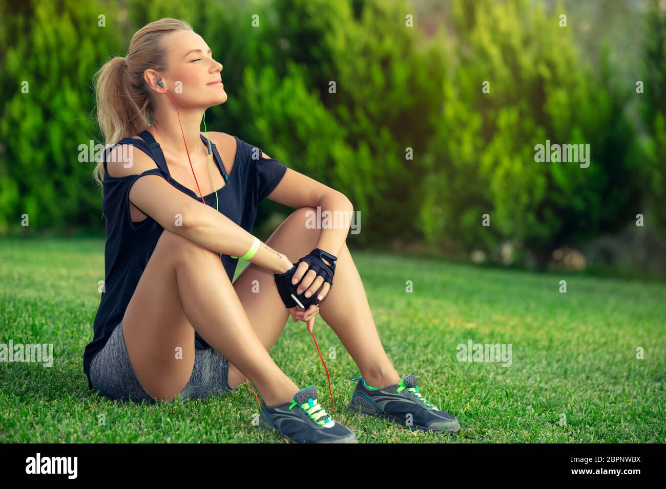 Schöne athletische Frau ruht auf grünem Rasen nach einem guten Training, Solarium und bei Musik, Harmonie und Seele balance Konzept Stockfoto