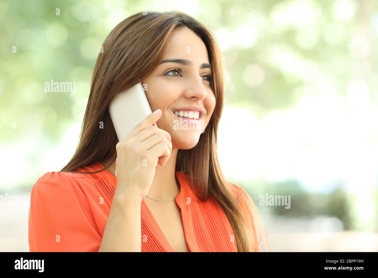 Smiley Frau in orange am Telefon sprechen oben in einem Park suchen Stockfoto