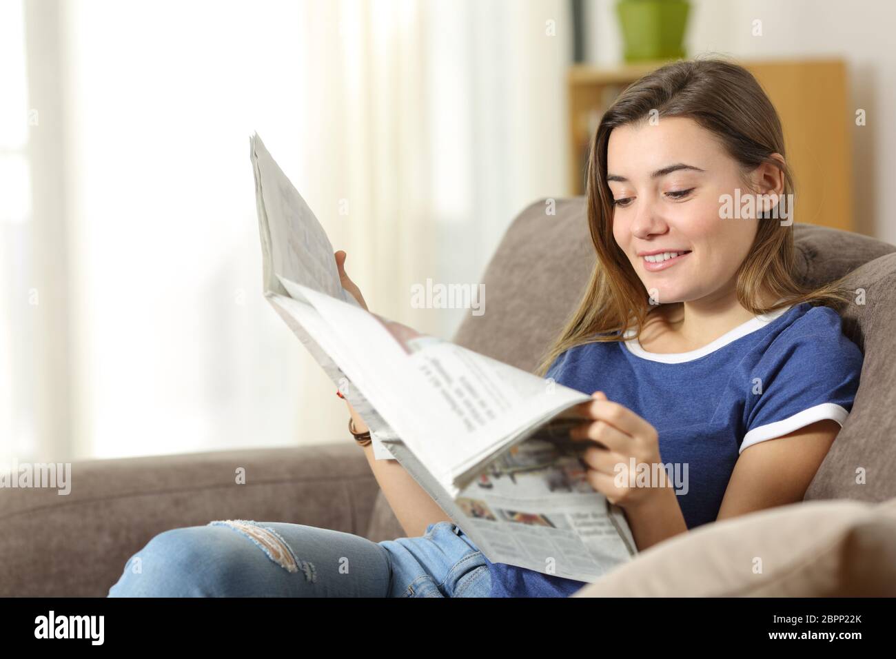 Happy Teen Reading eine Zeitung sitzt auf einem Sofa im Wohnzimmer zu Hause Stockfoto