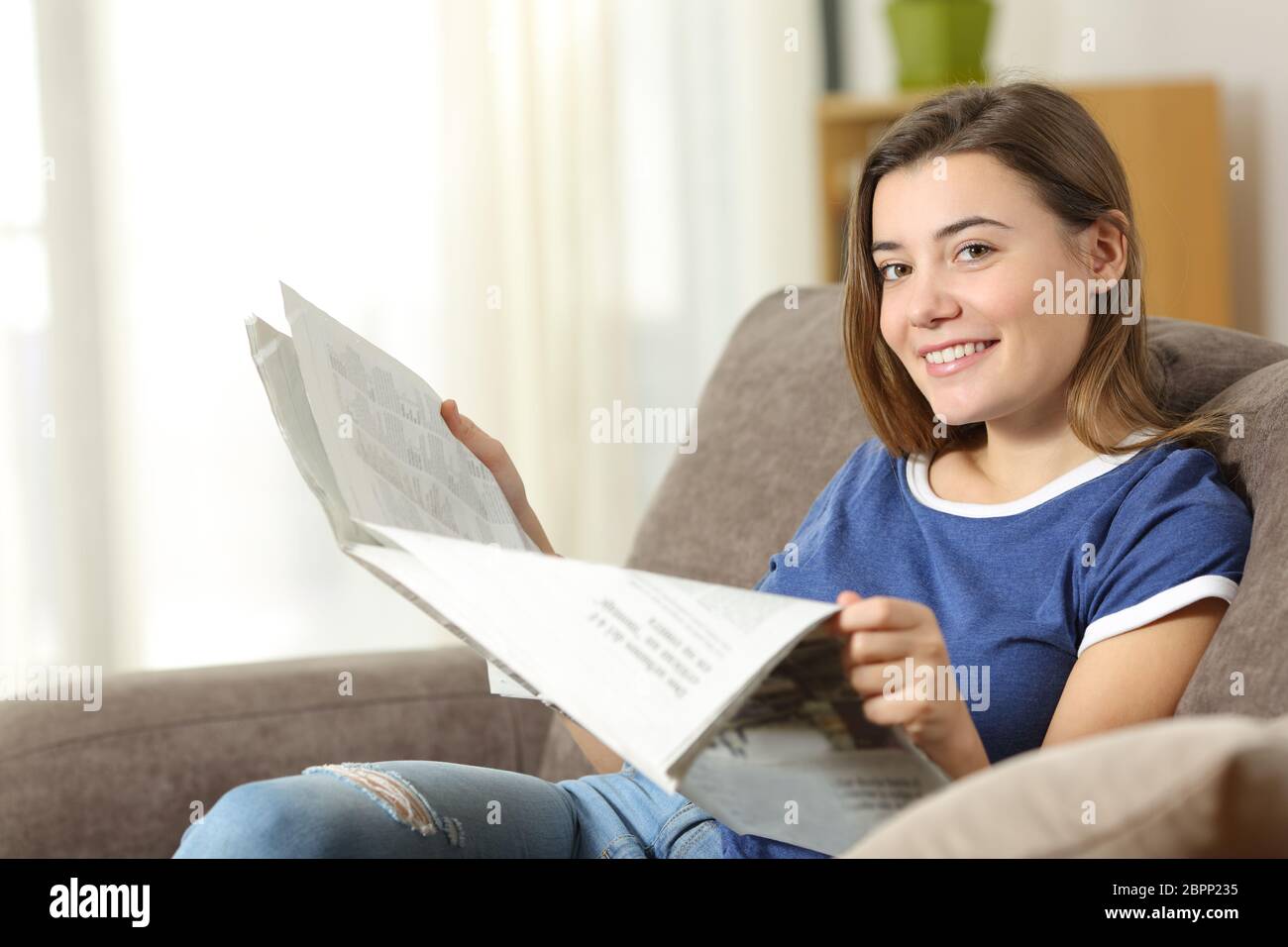 Teen Reading eine Zeitung an der Kamera sitzt auf einer Couch im Wohnzimmer zu Hause suchen Stockfoto