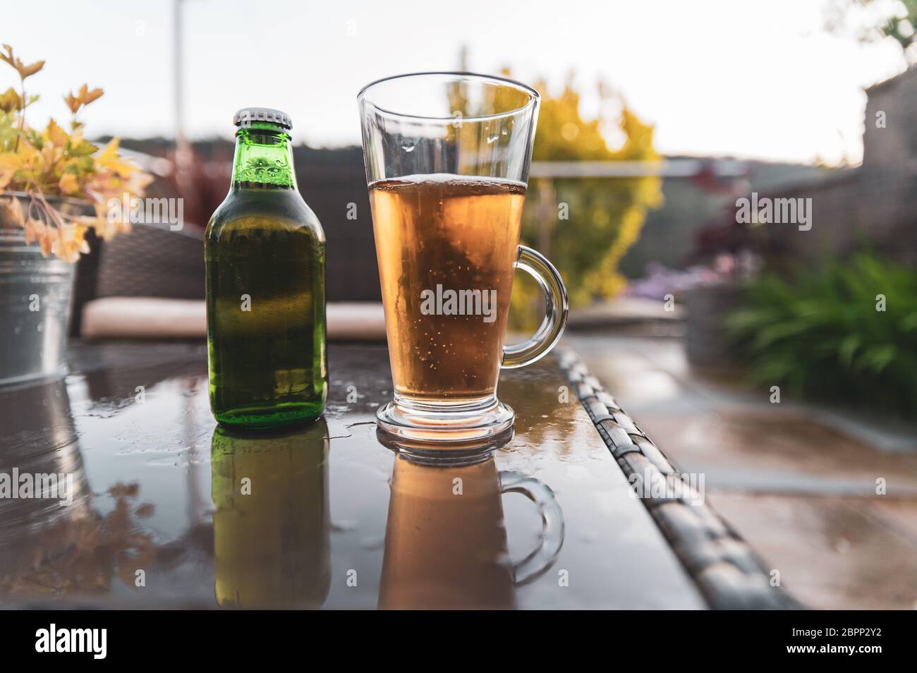 Frisches Bier in Glas auf Gartentisch mit Blick auf die Gartenlandschaft in einer flachen Tiefe des Feldes, verschwommener Hintergrund gegossen. Stockfoto