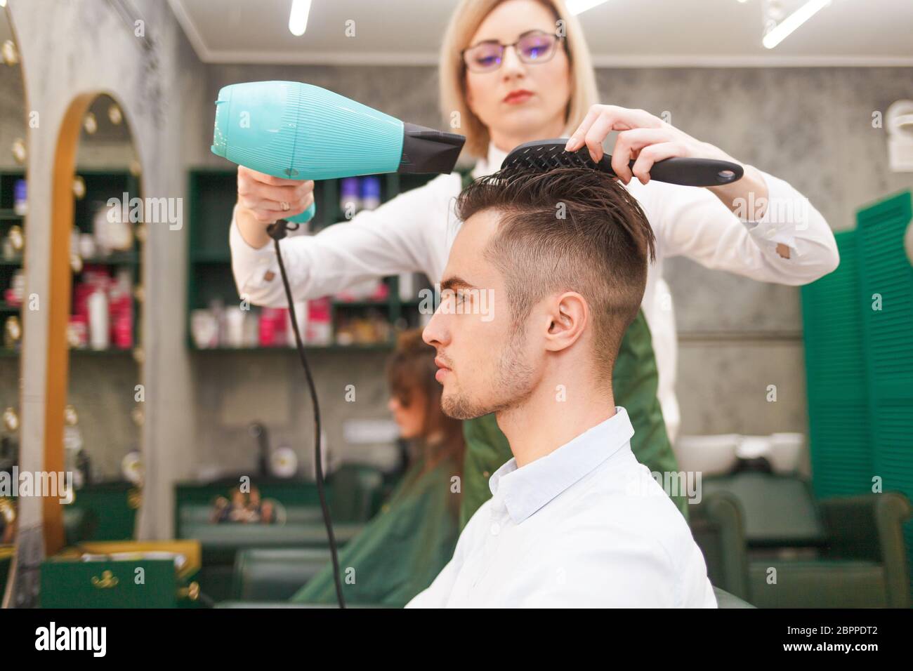 Friseur trocknet Haare von stilvollen Mann. Junge gutaussehende Kerl tun Haar Styling bei einem Friseur Stockfoto