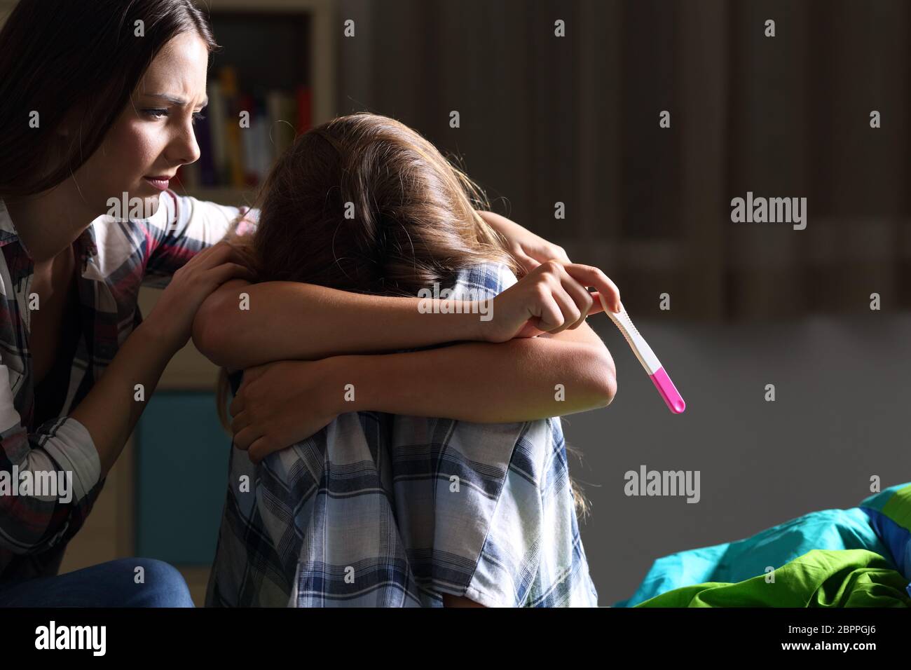 Schwester beruhigend, eine schwangere traurige Teen in ihrem Schlafzimmer mit einem dunklen Licht im Hintergrund Stockfoto