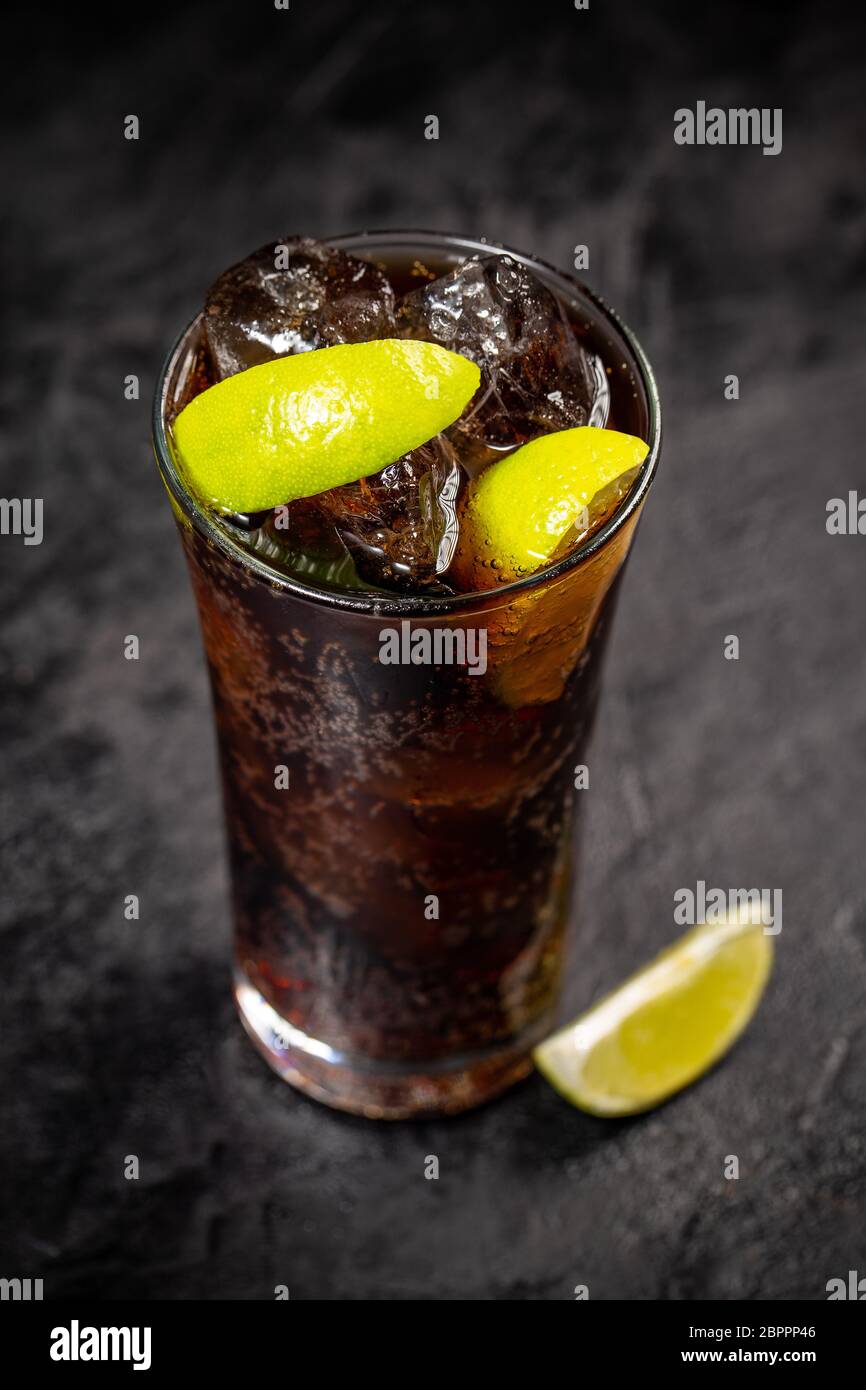 Frischen Cuba Libre mit brauner Rum, Cola und Zitrone auf schwarzem Hintergrund Stockfoto