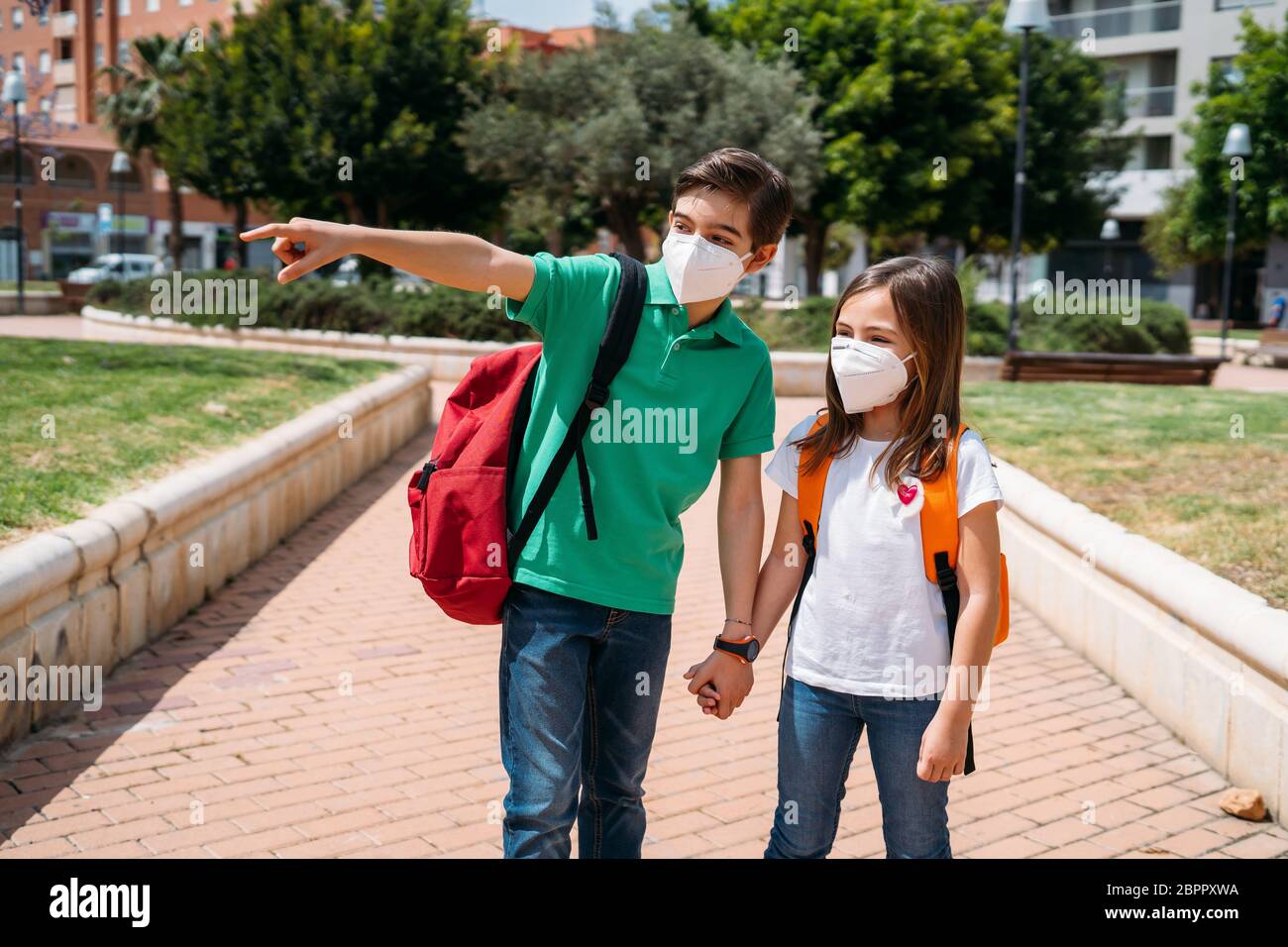 Junge und Mädchen mit Rucksäcken und Masken gehen zur Schule in Coronavirus Pandemie Stockfoto