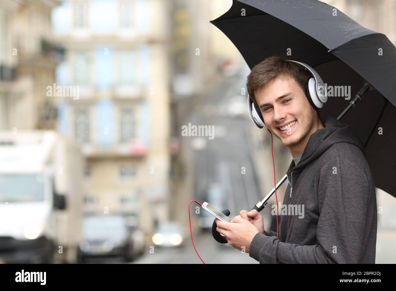 Happy Teen Musik hören mit Kopfhörern an Suchen Sie auf der Straße unter dem Regen Stockfoto