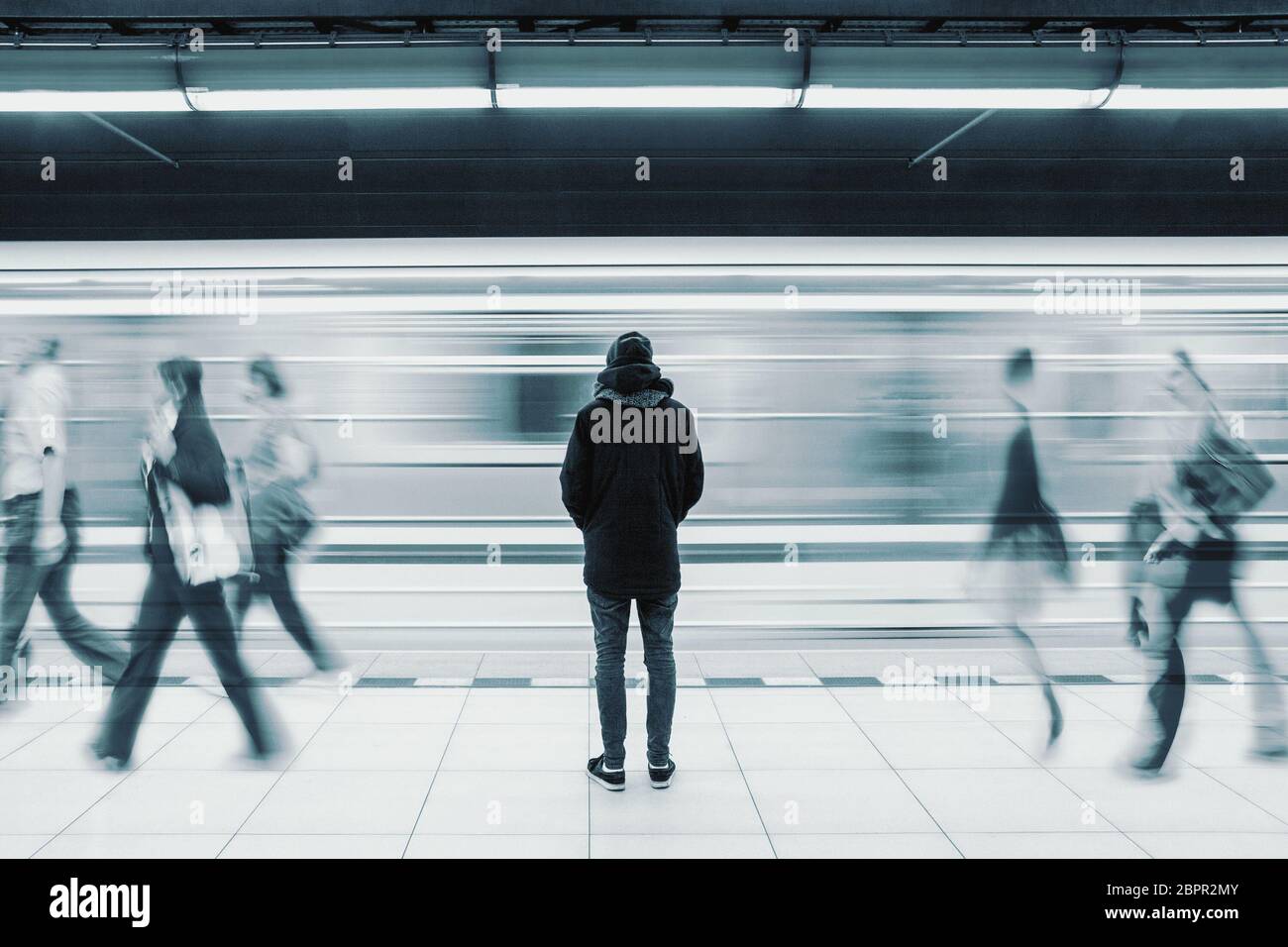 Lange Belichtung Bild mit einsamen Jungen Mann erschossen, von hinten an der U-Bahn station mit verschwommenen fahrenden Zug und nur wenige Leute im Hintergrund Stockfoto