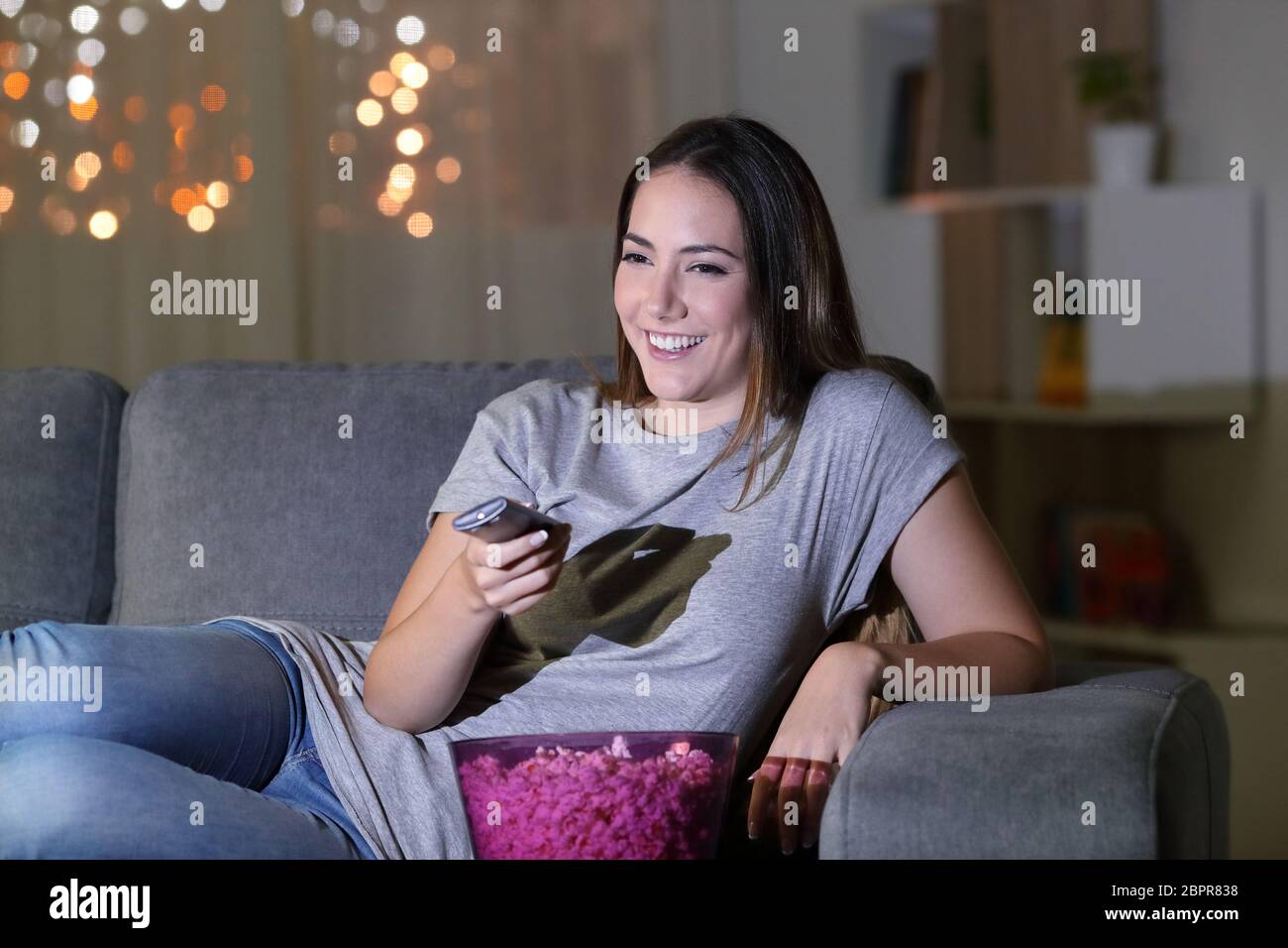 Glückliche Frau Fernsehen Inhalt in der Nacht auf einer Couch im Wohnzimmer zu Hause sitzen Stockfoto