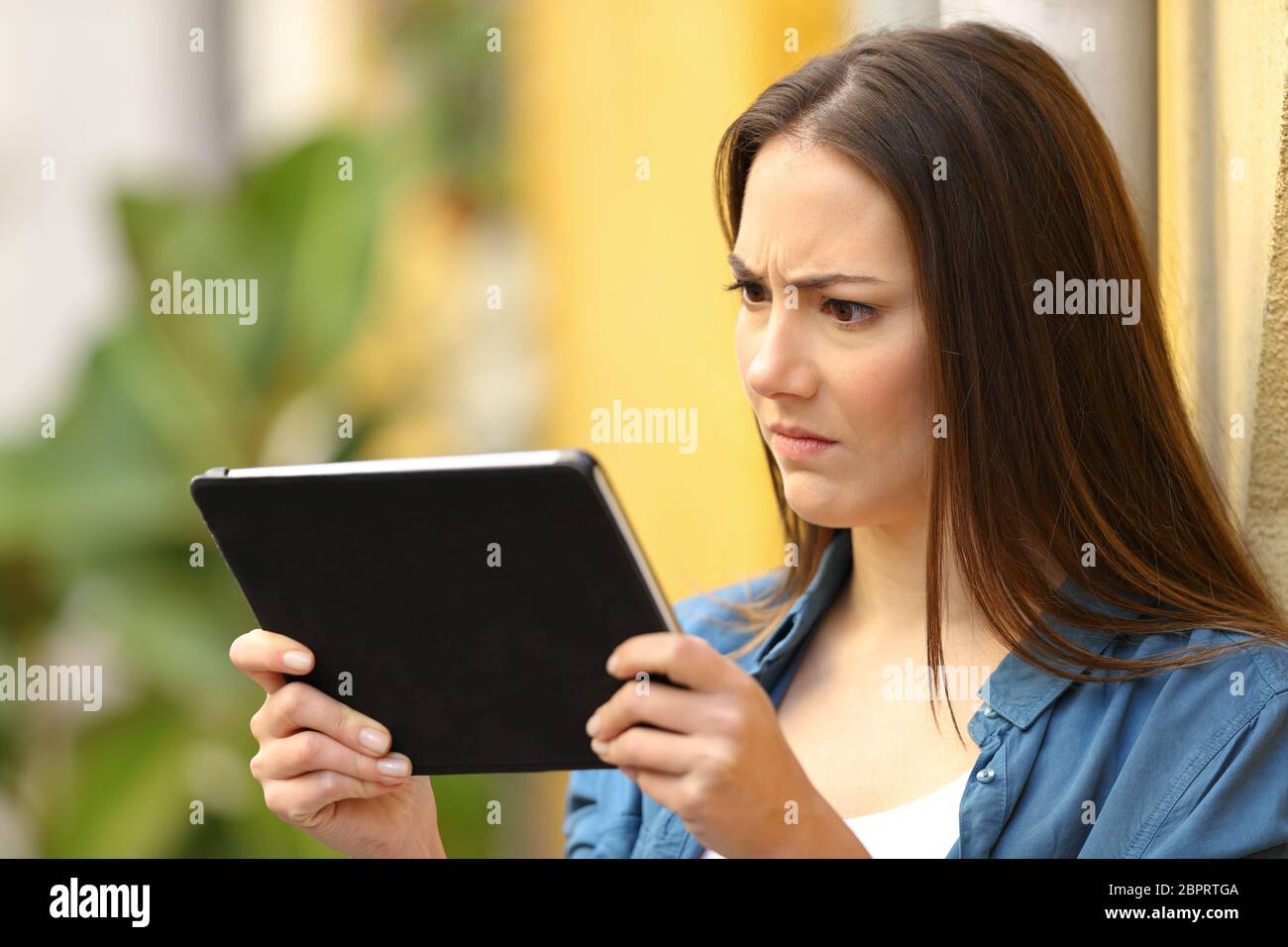 Wütende Frau ist Kontrolle tablet online Inhalte in eine bunte Straße Stockfoto