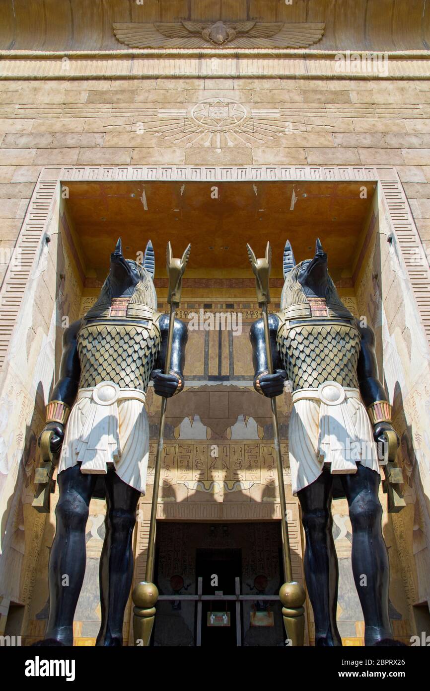 Zwei riesige Statuen des ägyptischen gottes Anubis - des gottes des Jenseits mit Schlagstöcken in den Händen bewachen den Eingang zum Gebäude. Ansicht von unten. Stockfoto
