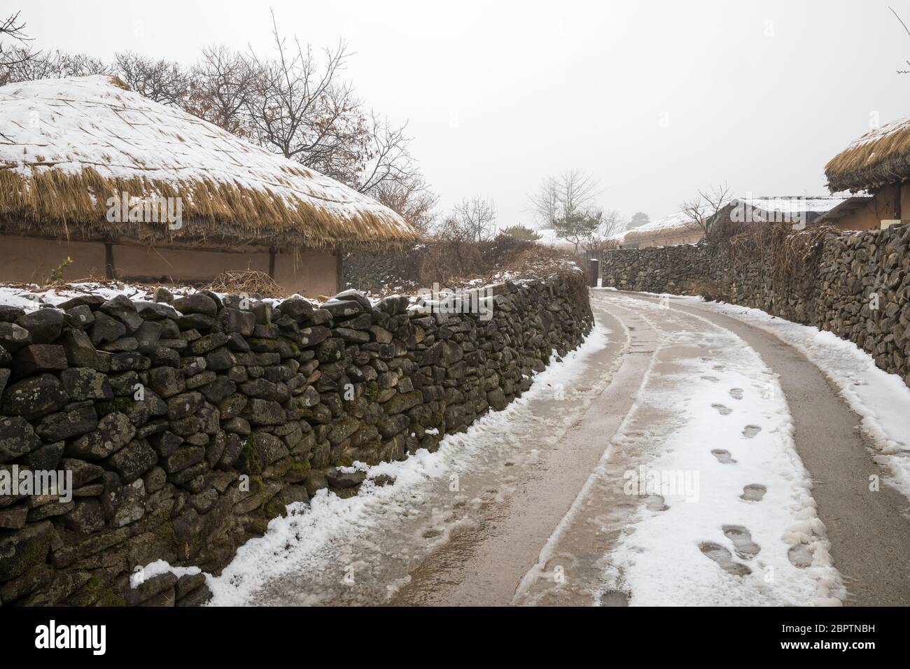 Koreanischer Winter, die Straße zwischen traditionellen schneebedeckten Dörfern und Steinmauern. Stockfoto