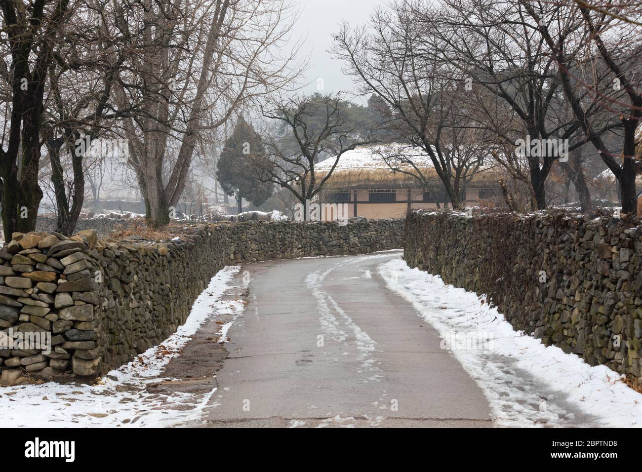 Koreanischer Winter, die Straße zwischen traditionellen schneebedeckten Dörfern und Steinmauern. Stockfoto
