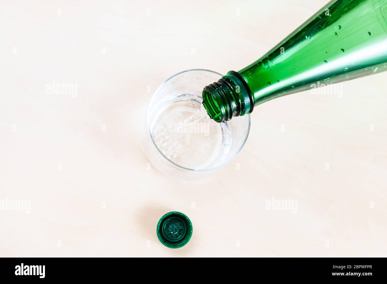 Draufsicht von Gießen Mineralwasser aus grünen Kunststoff-Flasche in Glas auf hellbraunen Tisch Nahaufnahme Stockfoto