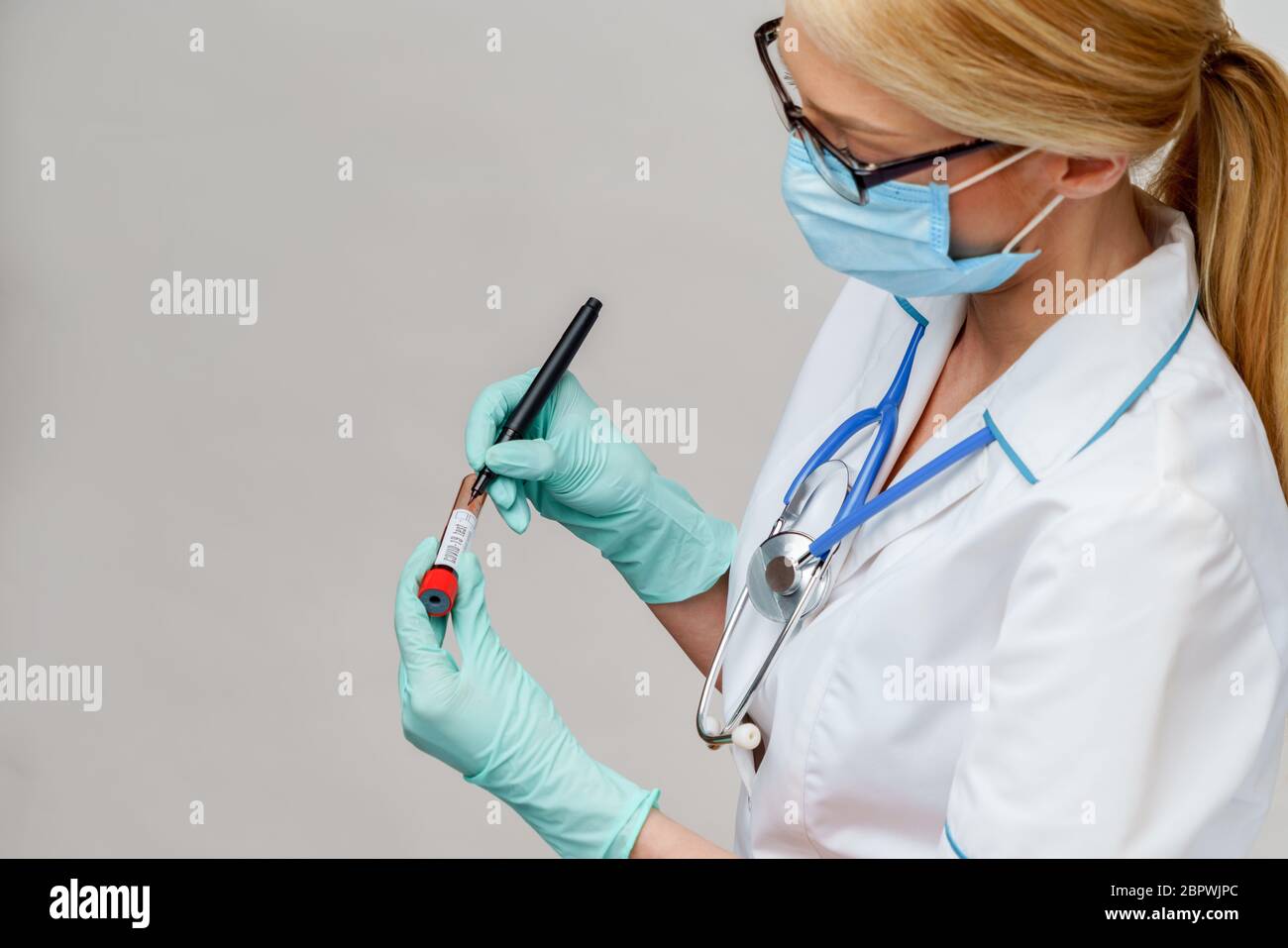 Arzt Krankenschwester Frau trägt Schutzmaske und Handschuhe - Marke mit Stift auf Virus Blut Teströhrchen Stockfoto