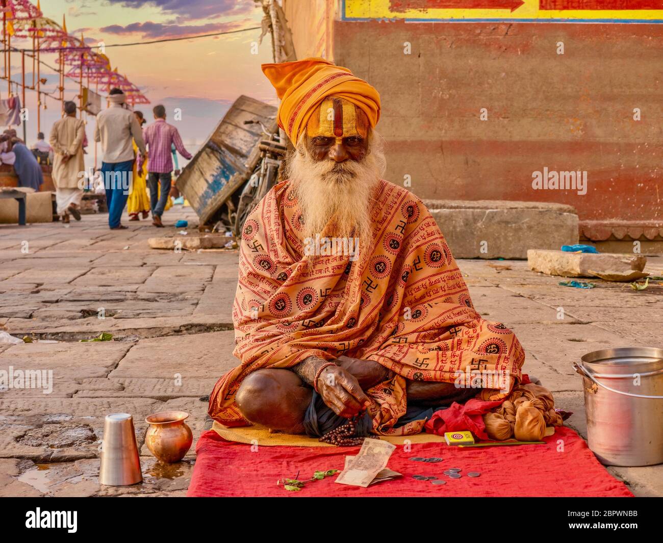 Varanasi, Indien - 13. November 2015. Ein älterer Sadhu sitzt auf einer Matte in der Nähe des Ganges River Ghats, trägt traditionelle Kleidung und Hindu-Stirnmarkierungen. Stockfoto