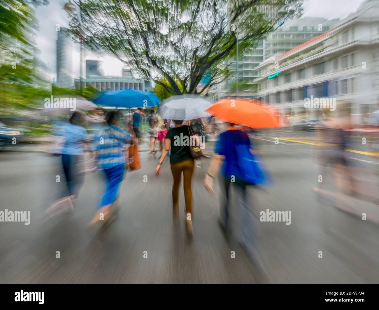 Eine Bewegungsunschärfe, bei der Fußgänger an einem regnerischen Tag in der Innenstadt von Singapur eine Straße überqueren. Rasantes Stadtleben. Stockfoto