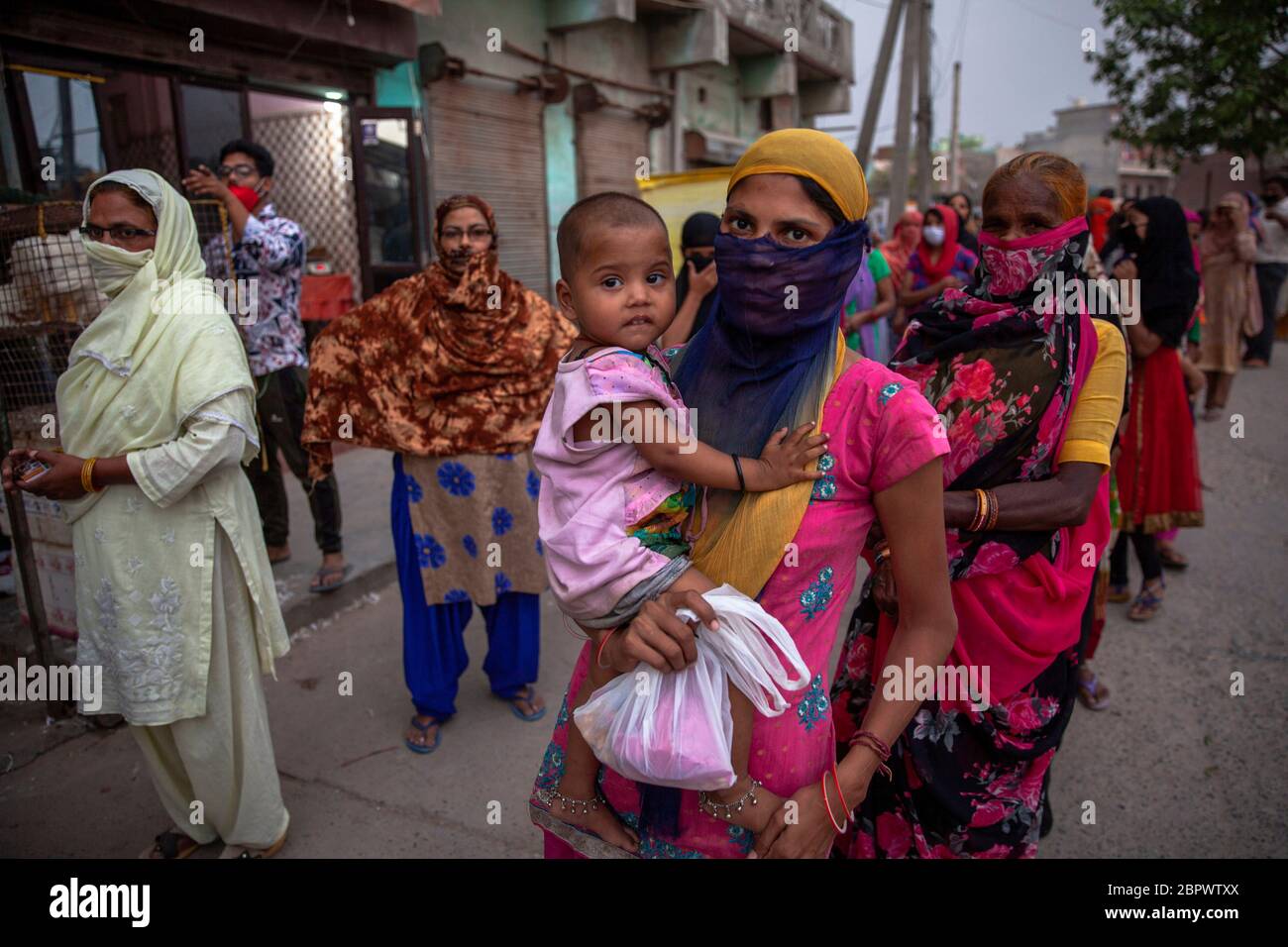 Indische Frauen warten auf kostenlose Nahrung in der Region Mustafabad, die kürzlich von Unruhen betroffen war, als das Land seine Lockdown-Beschränkung am 14. Mai 2020 in Neu-Delhi, Indien, lockert. Die Region Mustafabad gehörte zu den am schlimmsten betroffenen Gebieten, als im Februar in Indiens Hauptstadt Unruhen ausbrachen, weil ein umstrittenes Gesetz zur Änderung der Staatsbürgerschaft von der Regierung der Bharatiya Janata Partei verabschiedet wurde. Mehrere Familien, die aufgrund von Brandstiftung durch Randalierer obdachlos waren, kümmern sich nun um sich selbst inmitten einer landesweiten Lockdown, die von der Regierung auferlegt wurde, um die Ausbreitung des Coronavirus im Land einzudämmen. Zoll Stockfoto