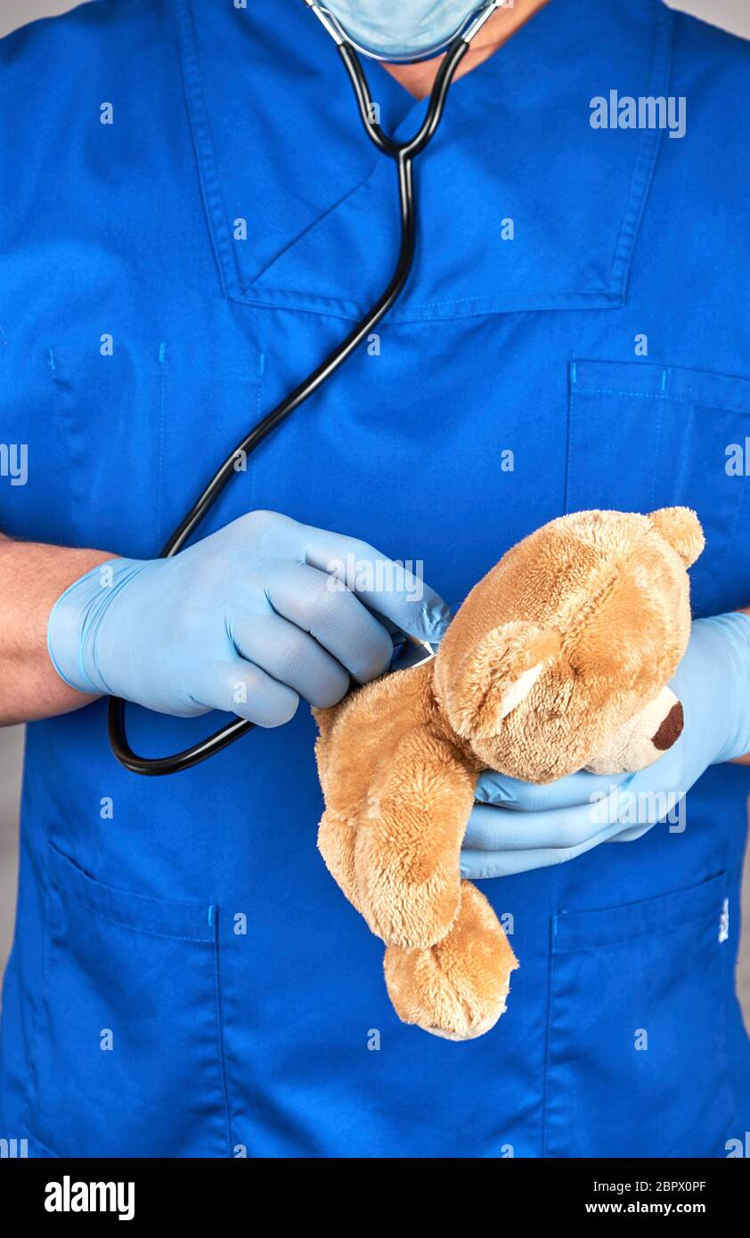 Arzt in der blauen Uniform und Latex Handschuhe mit einem braunen Teddybär, Kinderarzt behandelt ein Spielzeug Stockfoto