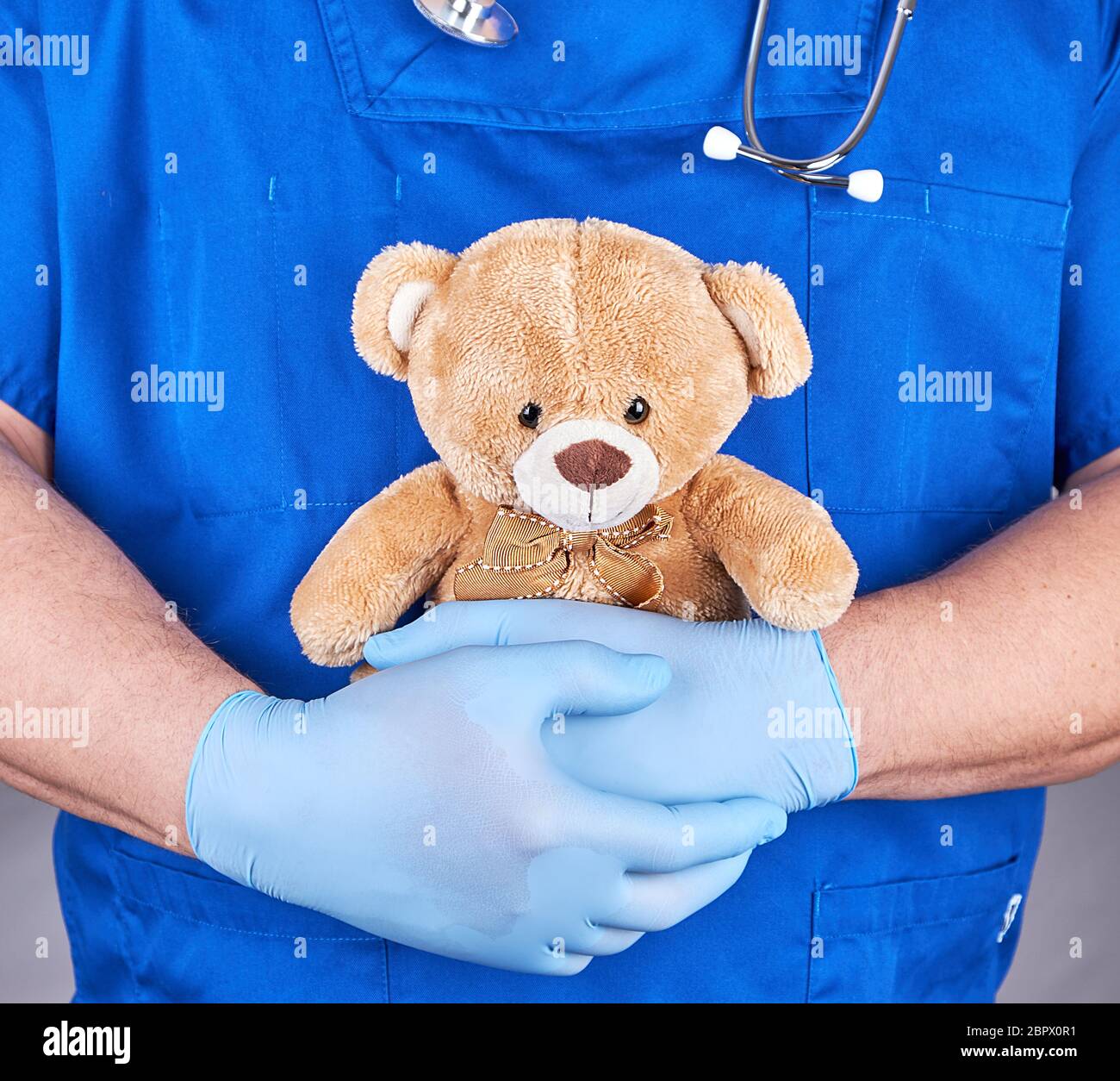 Arzt in der blauen Uniform und Latex Handschuhe mit einem braunen Teddybär, grauer Hintergrund Stockfoto