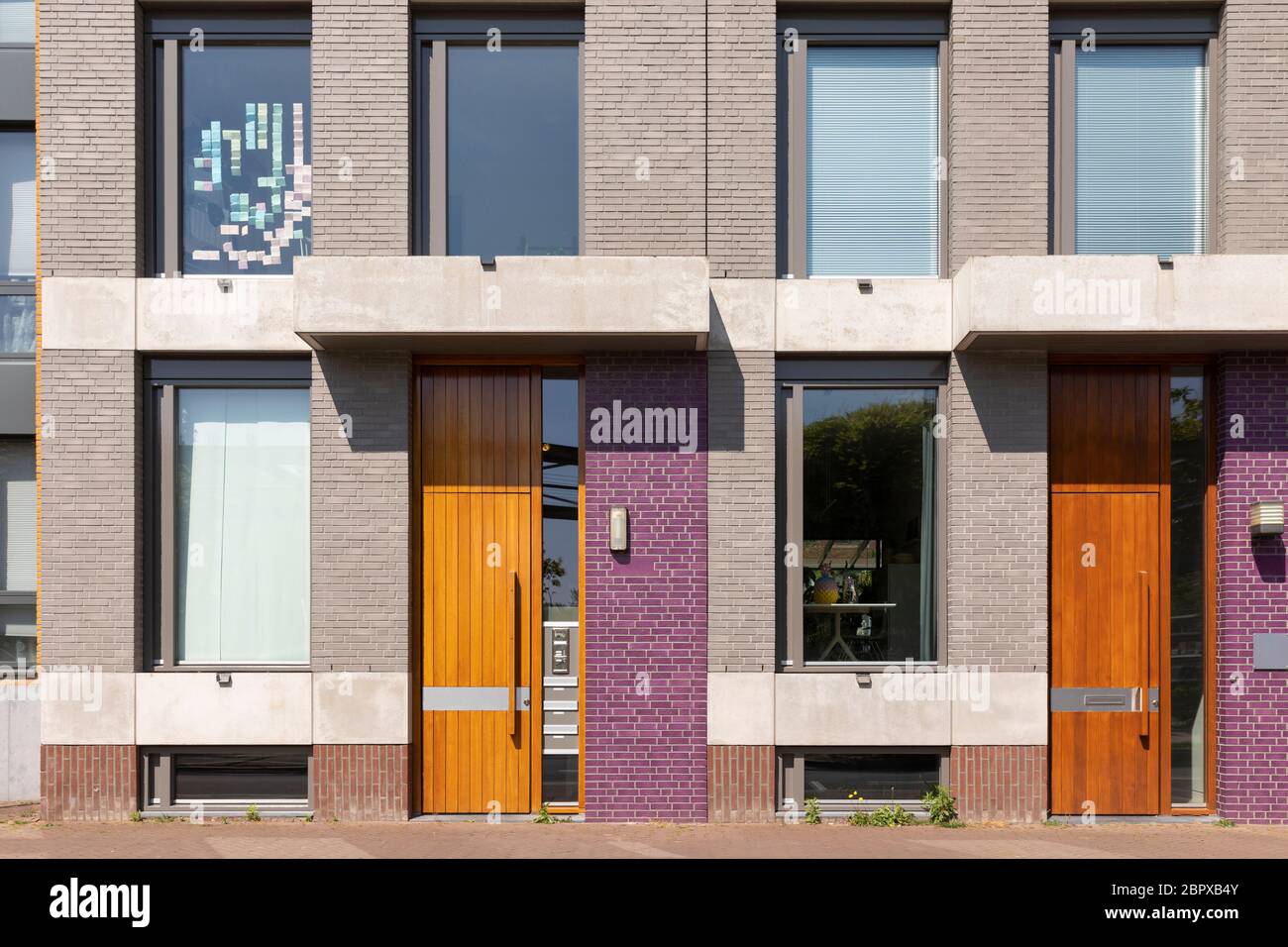 Außenfassade eines Hauses mit verschiedenen farbigen violetten Steinen und warmen braunen Holztüren. Moderne holländische Häuser in Brabant, Niederlande Stockfoto