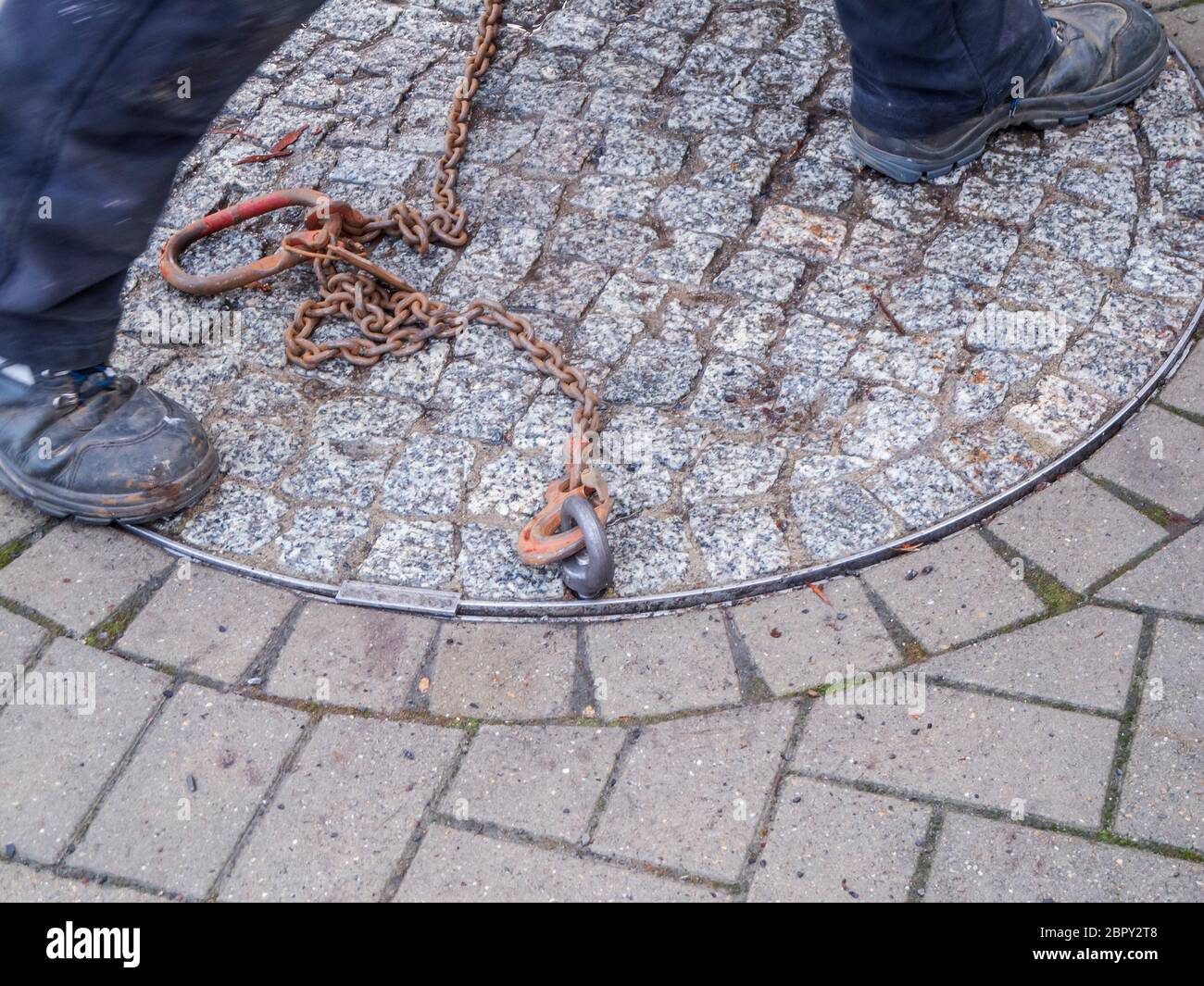 Unkenntlich städtischen Versorgungsarbeiter Eröffnung einer schweren doppelten Schachtabdeckung auf einer Straße mit Betonpflaster gepflastert Steine. Stockfoto