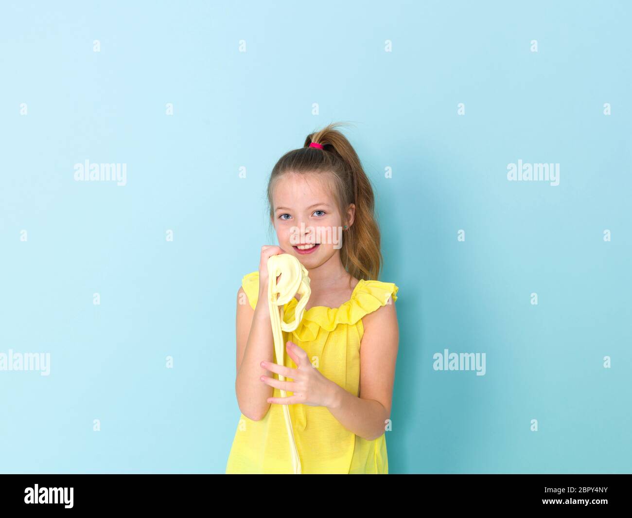 Wunderschönes 9-jähriges Mädchen spielt mit gelben Schleim vor blauem Hintergrund Stockfoto