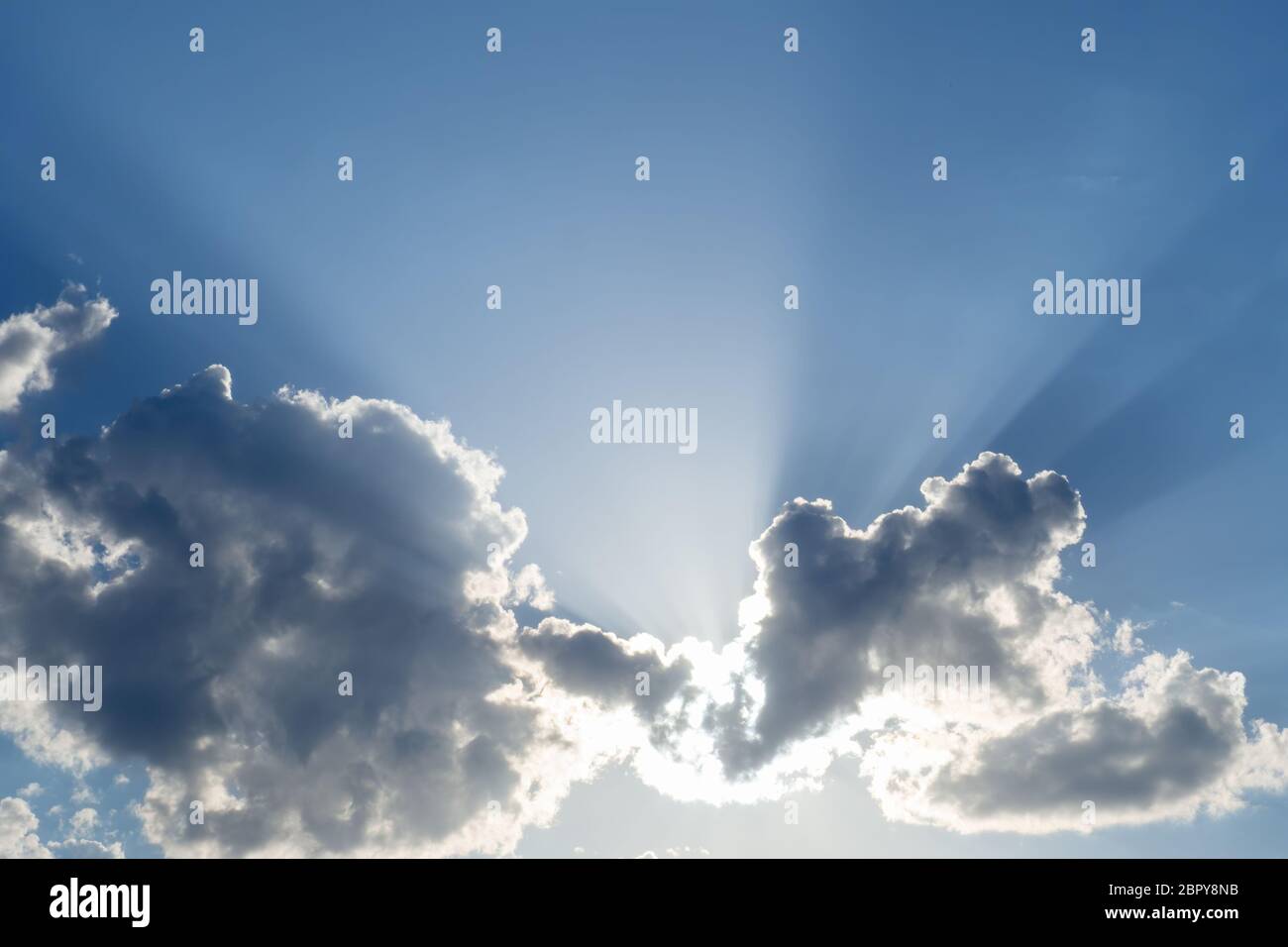Sonne scheint hinter den Wolken, Strahlen und Schatten am blauen Himmel. Kopierbereich Stockfoto