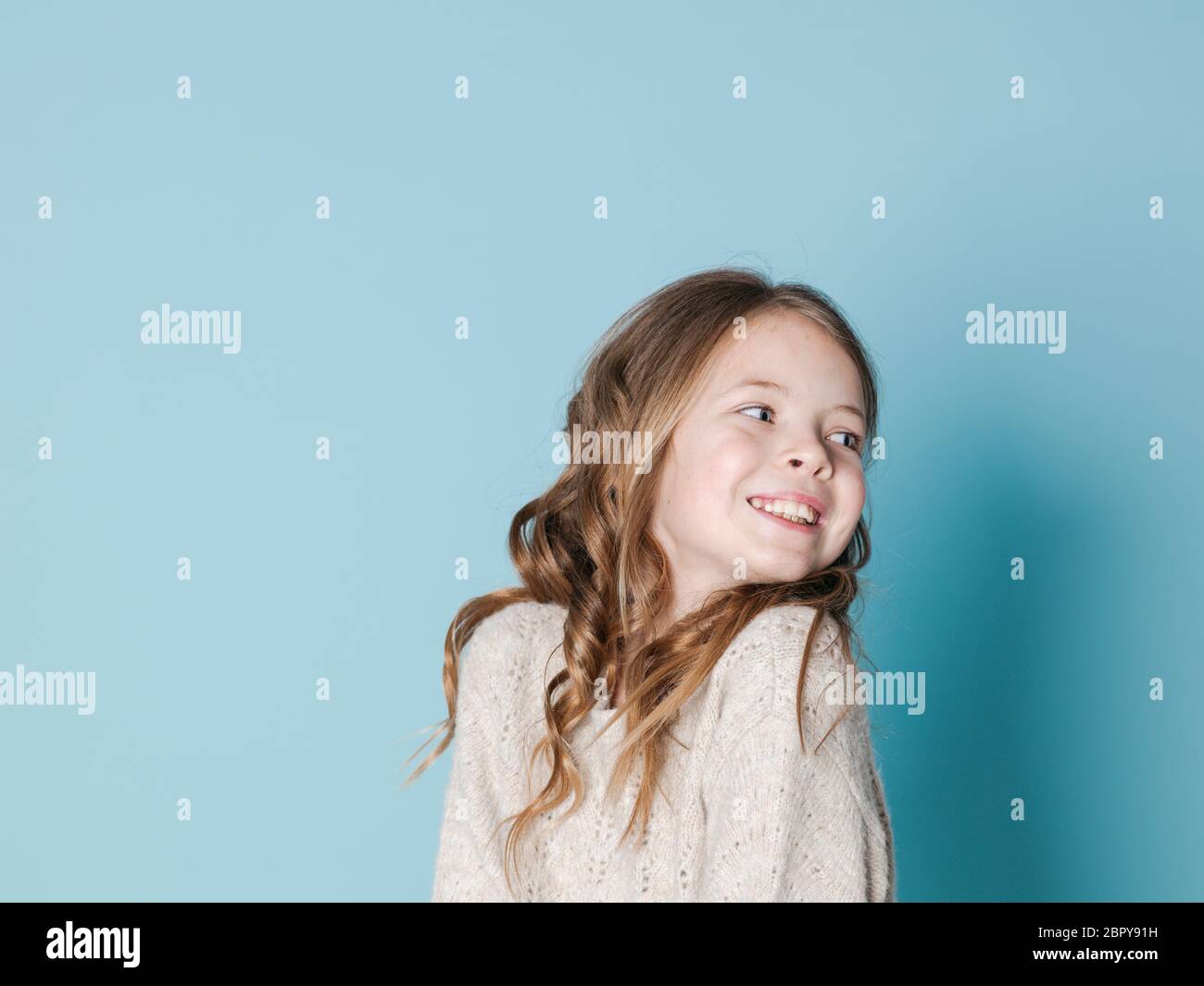 Hübsch und Cool 9 Jahre altes Mädchen mit braunen wolle Pullover vor blauem Hintergrund posiert Stockfoto