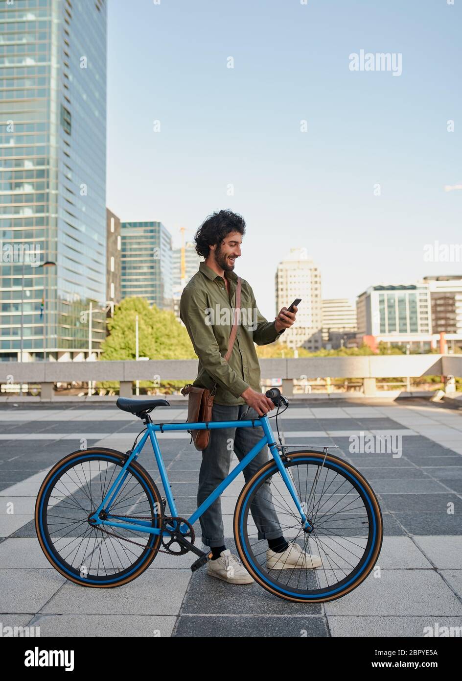 Side voller Länge Ansicht von schönen lächelnden Mann in formeller Kleidung auf der Terrasse mit Fahrrad mit Smartphone stehen Stockfoto