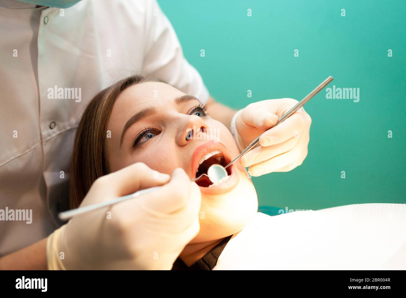 Junge Frau kam zum Zahnarzt zur Untersuchung. Der Zahnarzt untersucht den Patienten aus nächster Nähe Stockfoto