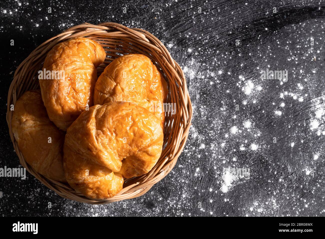 Von oben gesehen Croissants in einem Weidenkorb auf einem schwarzen Boden, die Gebäck Teig macht gelegt Stockfoto