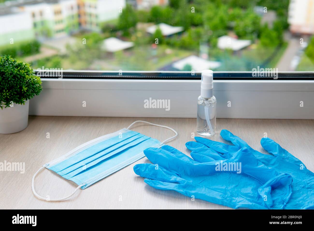 Blaue medizinische Handschuhe, Maske und antiseptisches Gel auf der Fensterbank Stockfoto