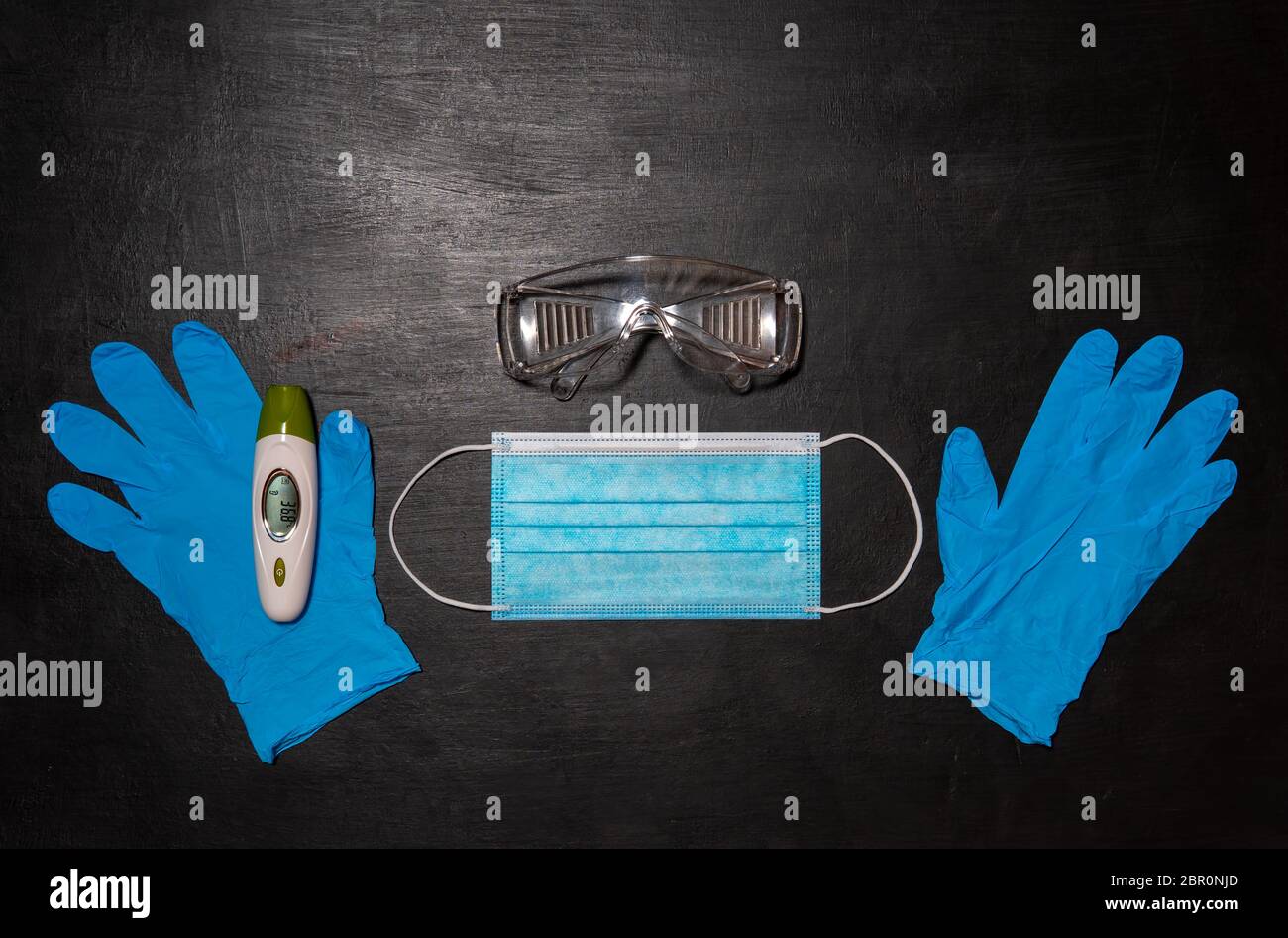 Schutzbrille, medizinische Maske, zwei blaue Handschuhe und Thermometer. Schwarzer medizinischer Hintergrund Stockfoto