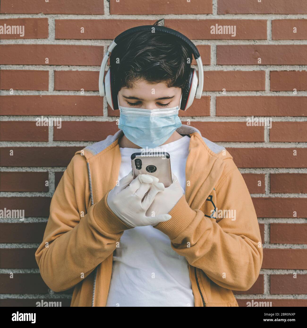 Kind trägt medizinische Maske mit Kopfhörer hört Musik mit seinem Smartphone im Freien Stockfoto
