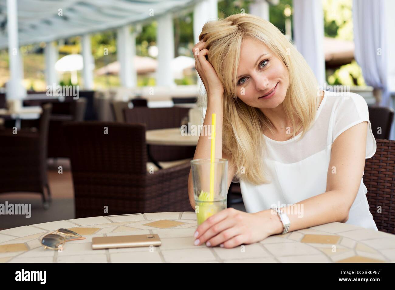 Schöne blonde Frau sitzt in einem Sommer-Café und trinkt Saft Stockfoto
