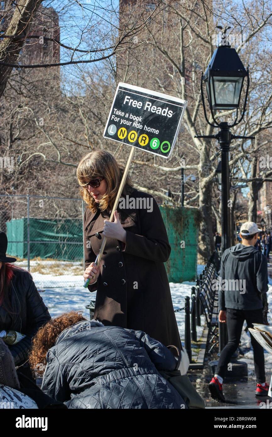 Frau mittleren Alters, die ein kostenloses Leseplakette hält und gebrauchte Bücher im Washington Square Park von Manhattan, New York City, USA verschenkt Stockfoto